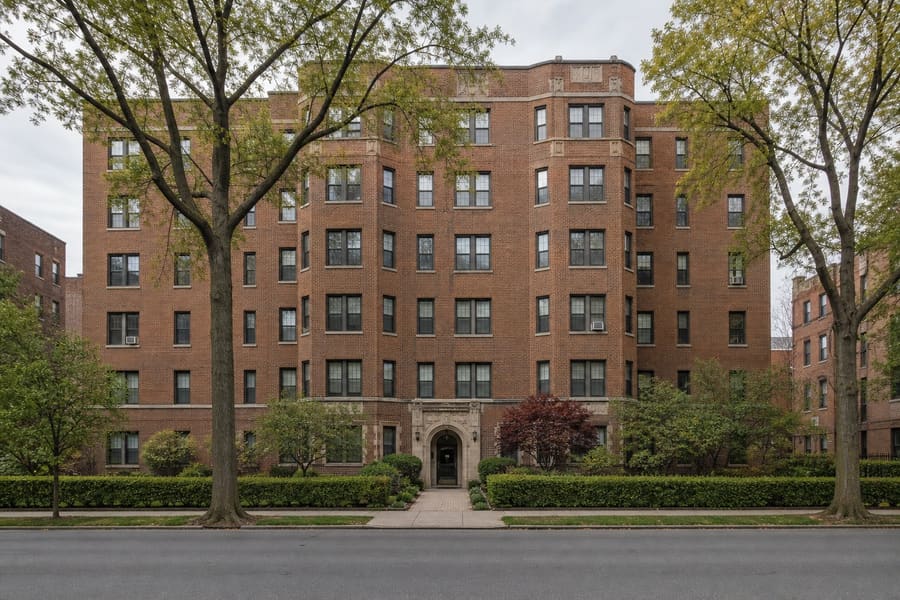 A prewar brick garden apartment building with an arched entrance and a planted forecourt